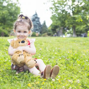 pretty-girl-sitting-green-grass-cuddling-her-teddy-bear_23-2147893054