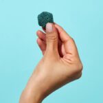 Kugel aus kleinen, blauen Perlen, die von einer Hand gehalten wird, vor einem hellblauen Hintergrund.