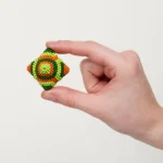 Buntes, kugelartiges Kunsthandwerk aus kleinen Perlen, gehalten zwischen Daumen und Zeigefinger.