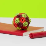 Bead model of a virus particle, made from colorful small beads, resting on a red notebook with a red marker nearby.