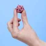 Bunte Perlenkugel, die auf einem kleinen Saugnapf auf einem menschlichen Zeigefinger haftet.