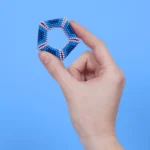 Hexagonale Magnetkugel-Struktur in Blau, Pink und Weiß, gehalten zwischen Daumen und Zeigefinger auf hellem blauen Hintergrund.