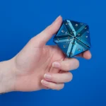 Metallischer Zauberwürfel mit Schrauben an der Hand, blauer Hintergrund.