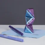 Kaleidoskopische Konstruktionsspielzeug aus metallischen, schimmernden Dreiecken in Blau und Lila, auf einem Notizblock mit Filzstiften.