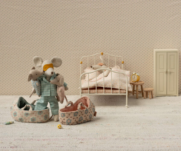 Puppenbett, Stofftiere und Bett mit Nachttisch in einem niedlichen Kinderzimmer im Vintage-Stil. Das Zimmer besitzt eine Tapete mit kleinen Punkten, eine weiße Metallbettwäsche, eine kleine Nachttischlampe und ein kleines Kleidungsset für die Puppen. Eine gemütliche und liebevoll gestaltete Spiel- und Schlafumgebung für kleine Kinder.