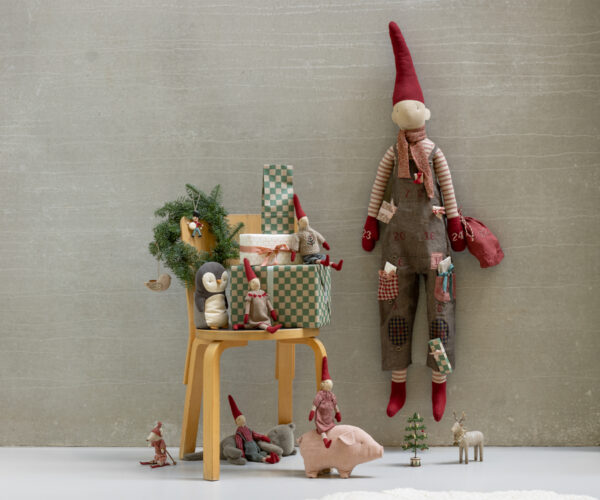 Weihnachtliche Dekoration mit Plüschfiguren, Geschenken und einem kleinen Weihnachtsbaum, die an einem grauen Wandhintergrund arrangiert sind.