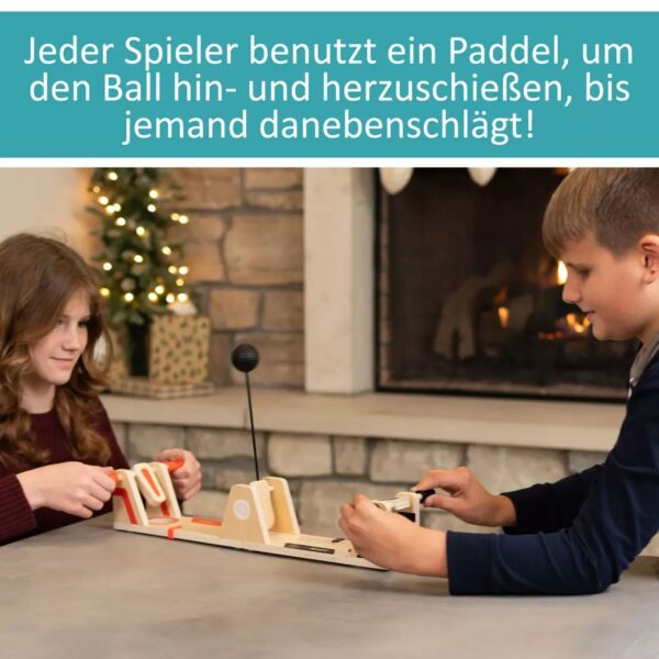 2. Mädchen und Junge spielen Flaschendrehen mit einem Tisch-Padell, während sie sich gegenseitig amüsieren, in einer gemütlichen Wohnzimmeratmosphäre mit Kamin und Weihnachtsbaum.